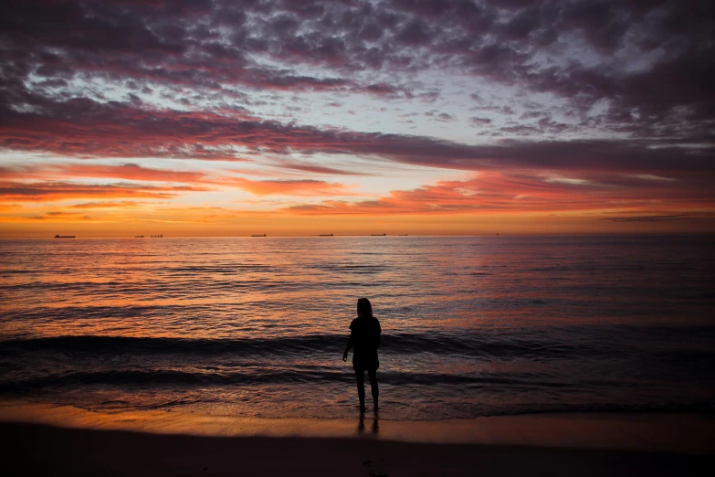 the woman is standing on the beach watching the sunset