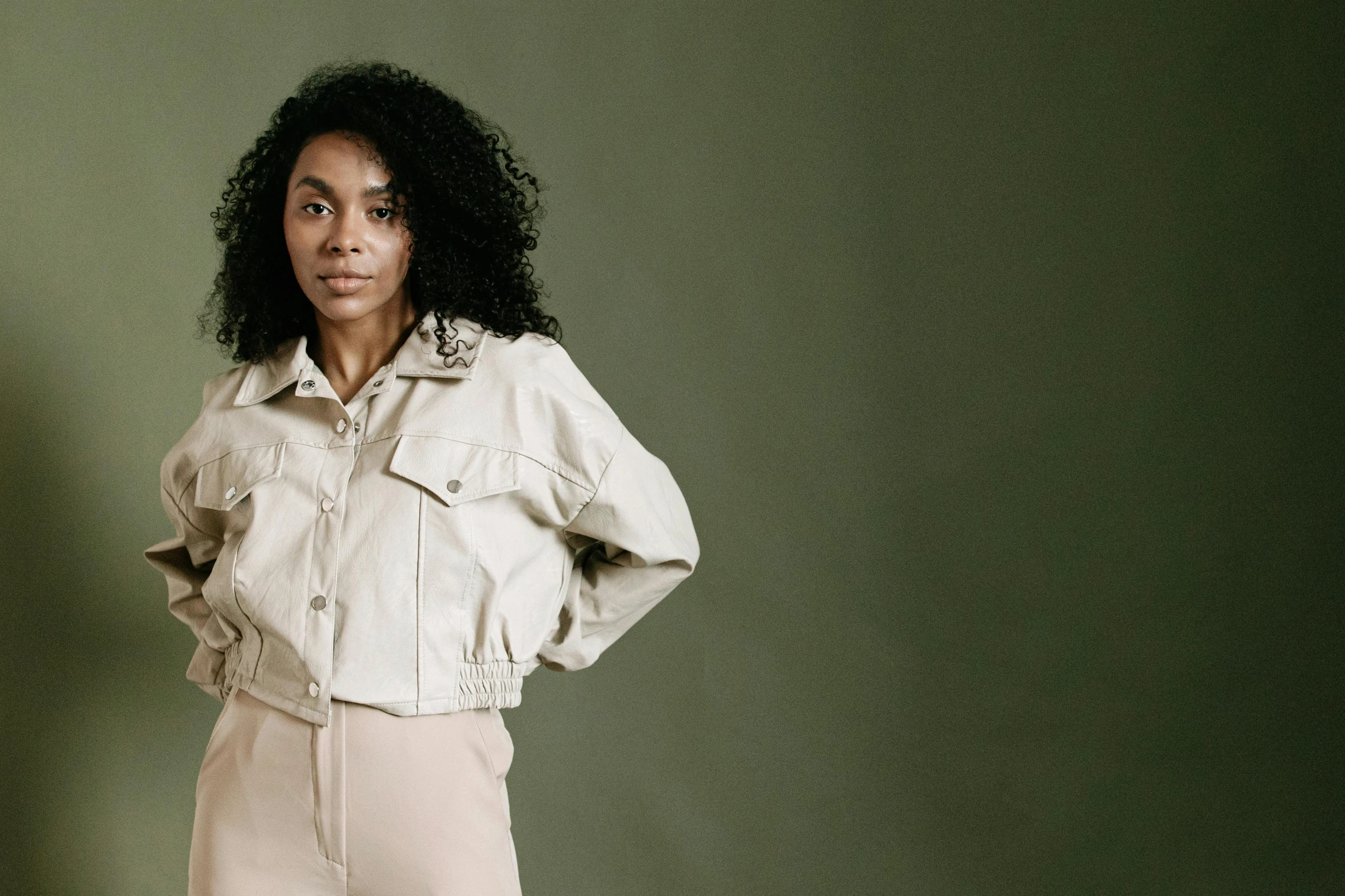 an african american woman with long black hair stands with her hands on her hips wearing white pants