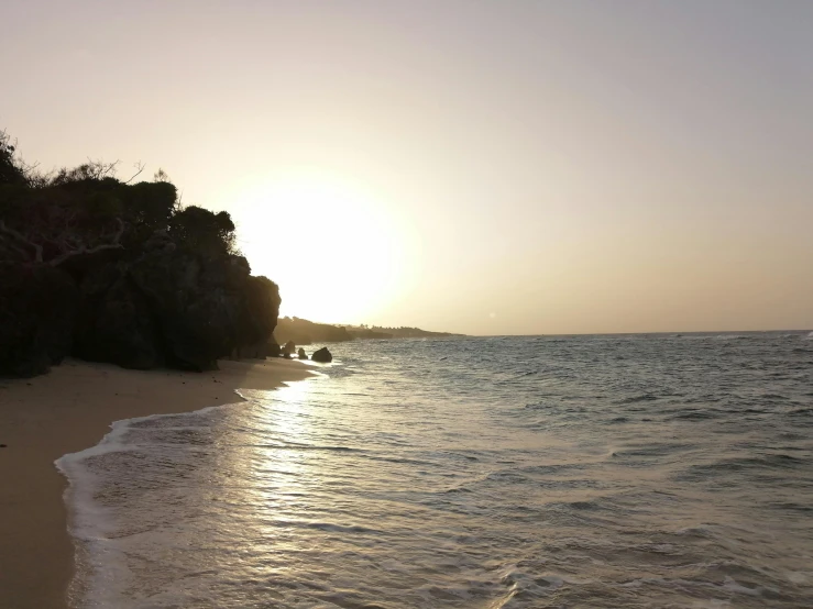 the sun sets over the ocean and reflects in the sand