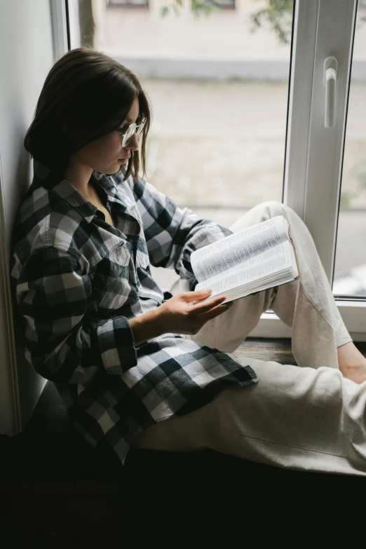 the girl is reading on the windowsill