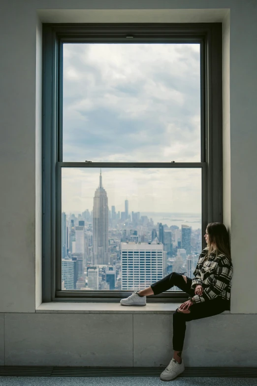 a woman sitting on the window sill looking out at city skyline