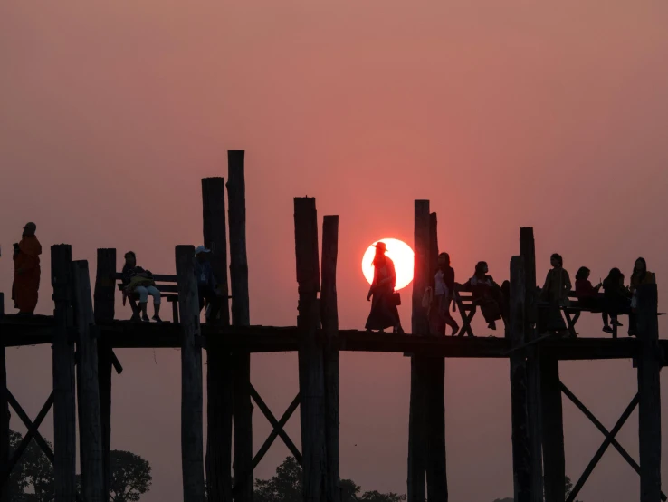 the sun is setting behind a group of people standing on a bridge