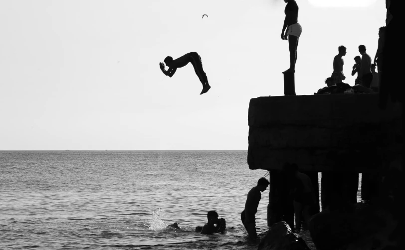 black and white po of group of people on pier jumping off ledge