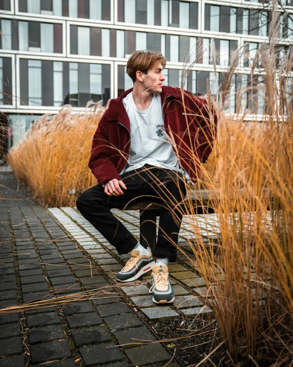 a young man sits on a stone bench in front of tall grass