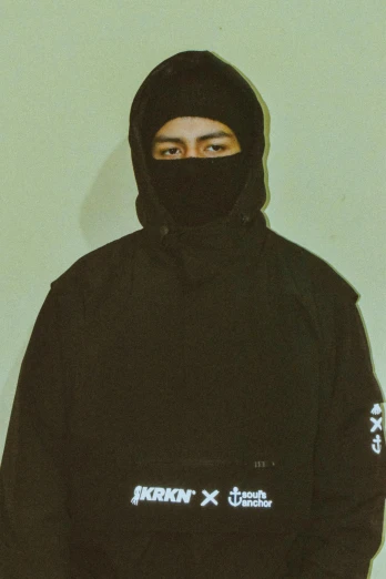 a man wearing black is standing in front of a wall with his head covered