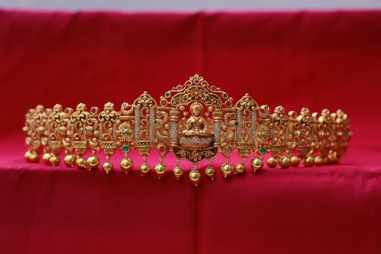 a gold tiara is displayed on a pink cloth