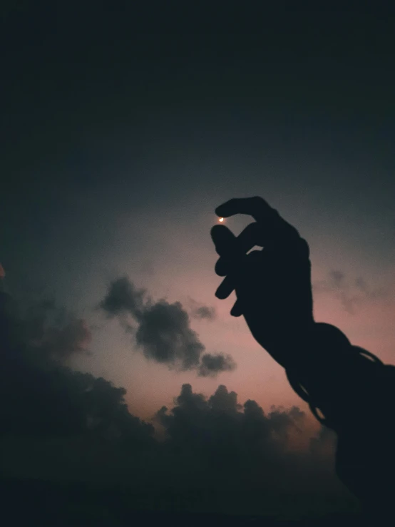 a person reaching up into the air at night with a sun setting in the background