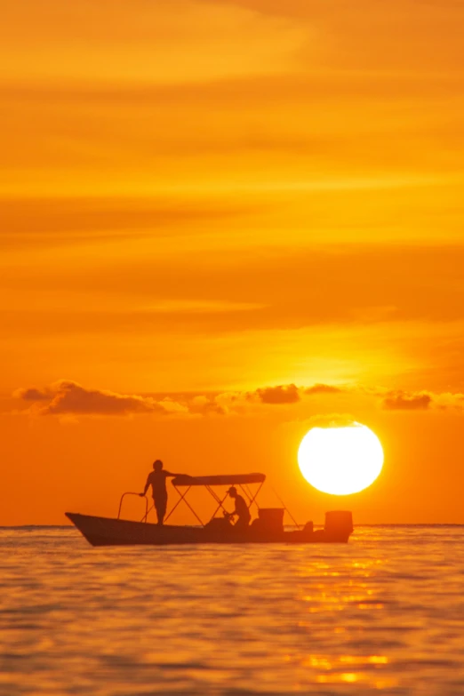 two people stand on the back of a small boat as the sun sets