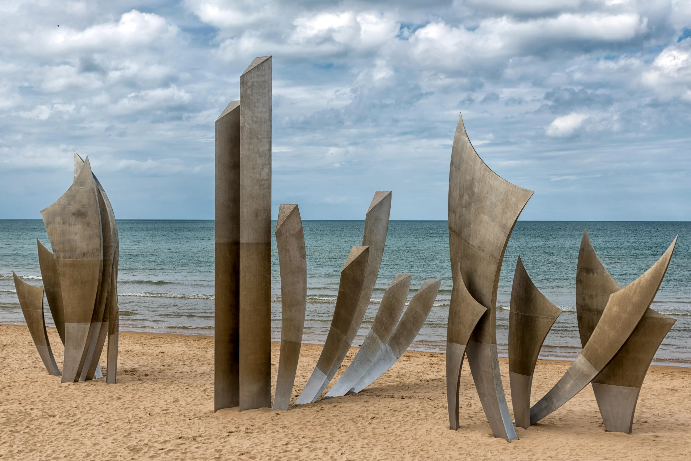 sculptures stand on the beach in front of the water