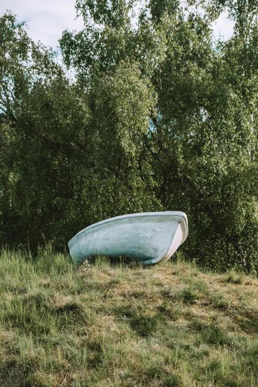 an old and worn boat sitting on the grass in front of some trees