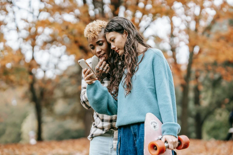 two woman are both looking at their cell phones