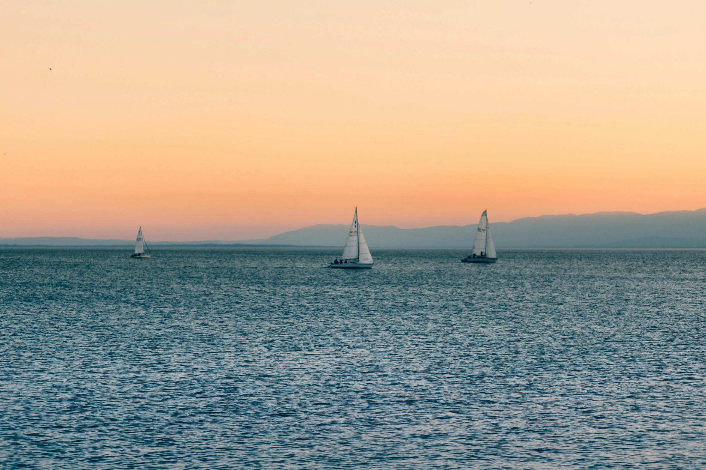 three boats are out in the ocean during sunrise