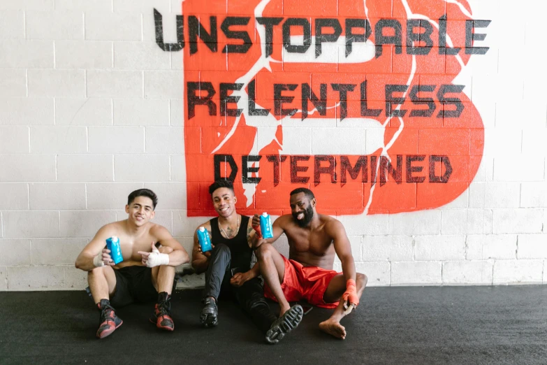 three young men sitting against a red sign