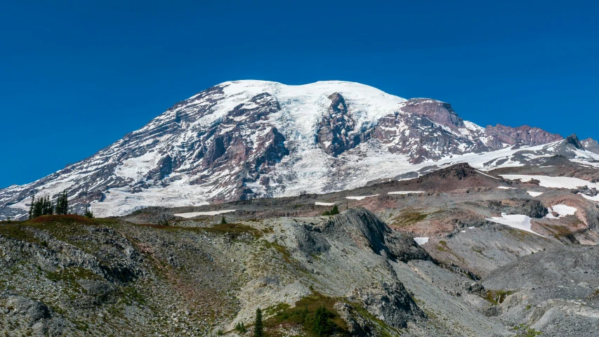 a mountain covered with snow covered rocks and surrounded by greenery