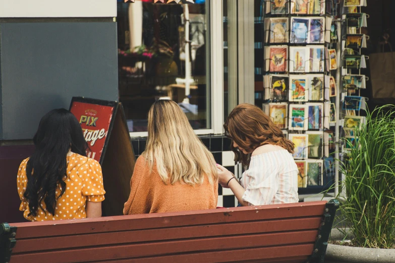 three woman sitting on a bench in front of a book store