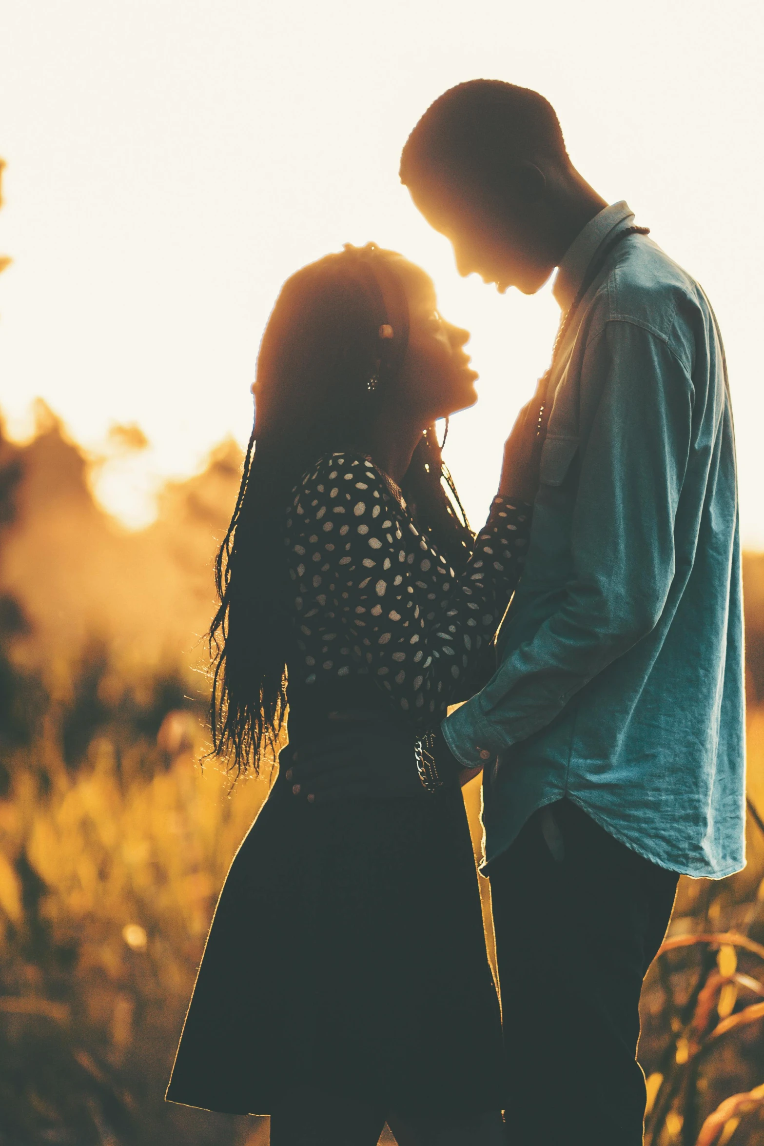 couple standing and hugging in an open field with sunlight shining on them