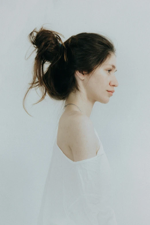  with hair in ponytail and white top over a blue wall