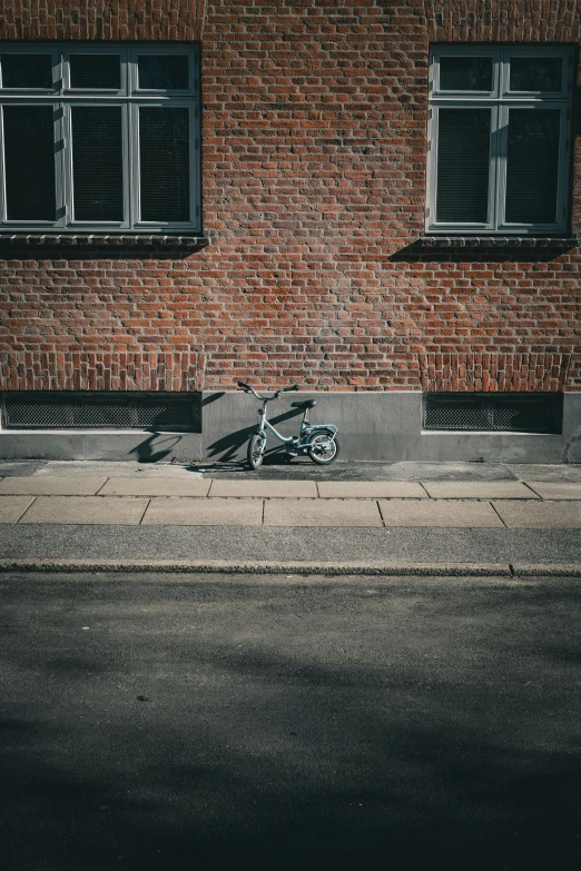 a bicycle sitting on a sidewalk in front of a brick wall