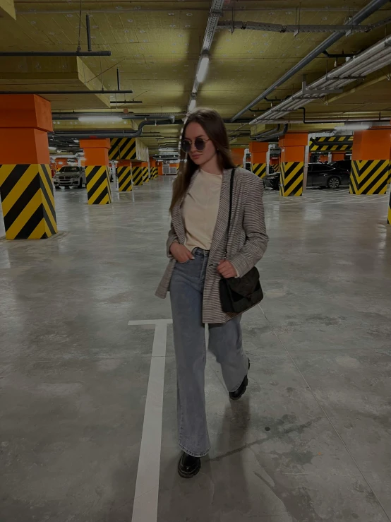 a woman in sunglasses is holding a bag and standing in an empty parking lot