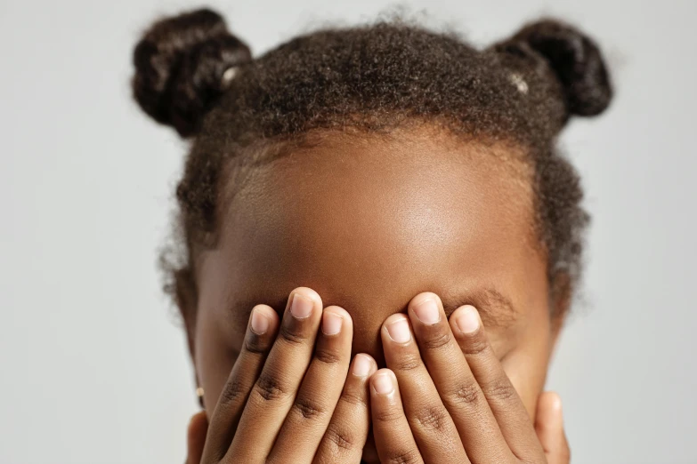 a close up view of an african american woman covering her eyes with both hands