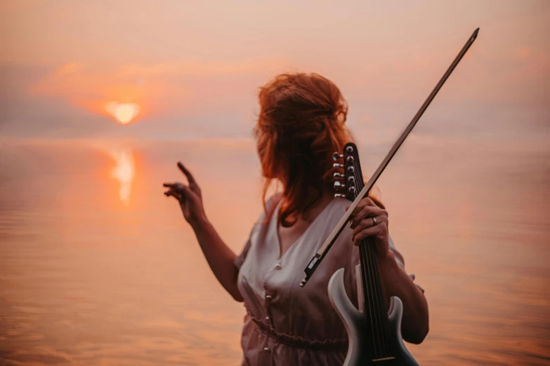 a beautiful young lady holding a guitar over water