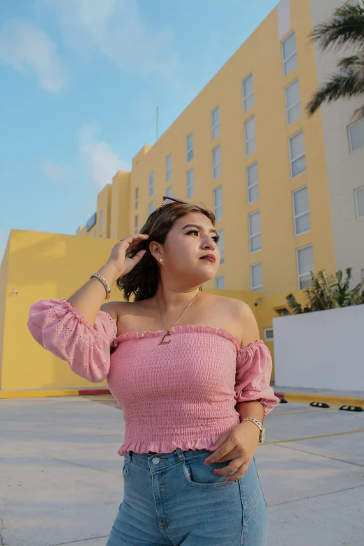 a young woman wearing jeans and a pink top is standing by a building