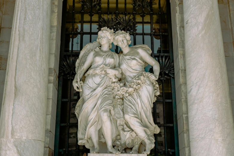 a statue with two women standing in front of a metal grate