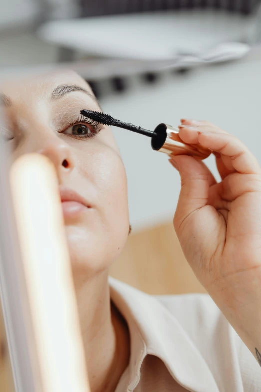 a woman has her eyeliner brush in front of the mirror