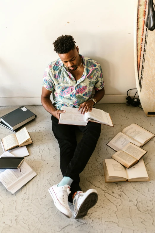 man sitting on floor with books near surfboard