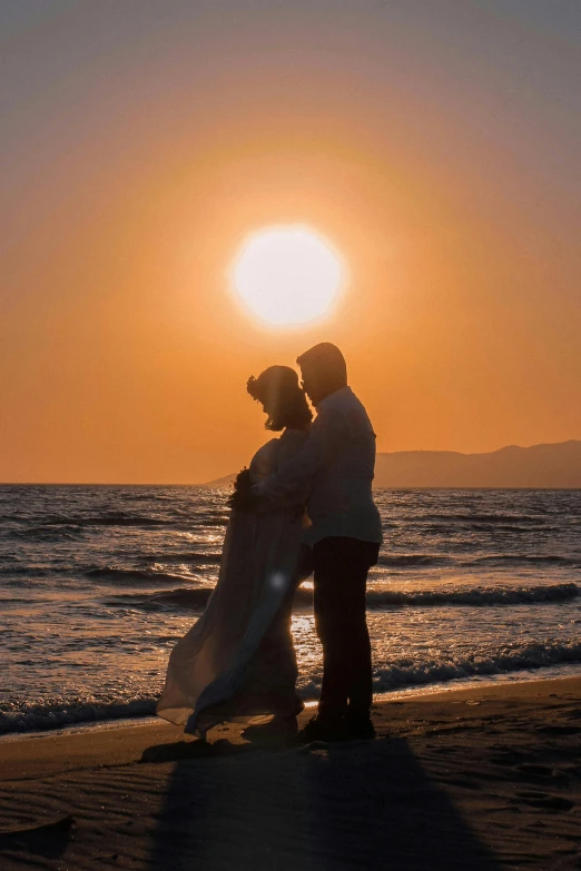 a couple posing for a picture in front of the sun at the beach