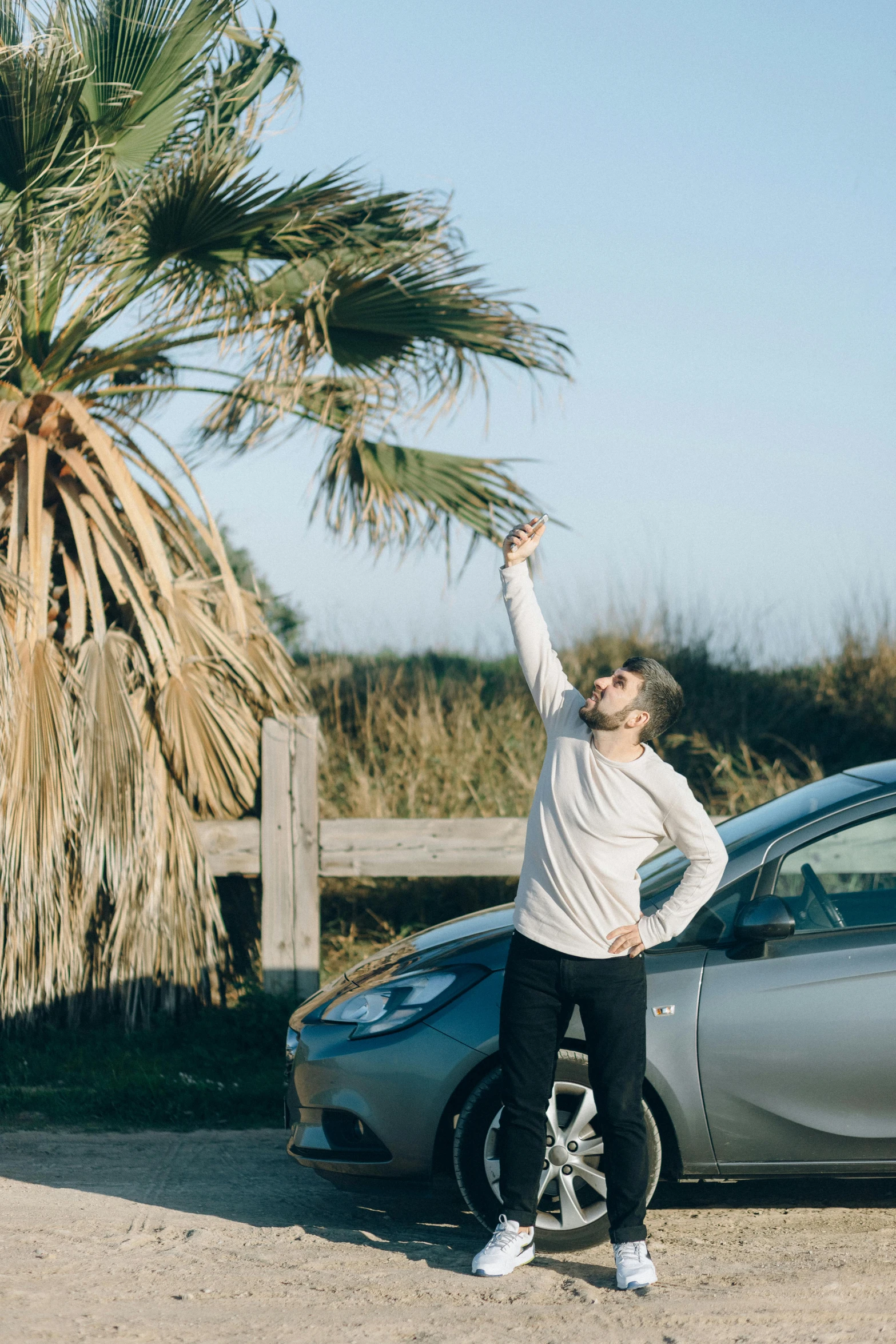 man standing near a parked car in front of palm tree