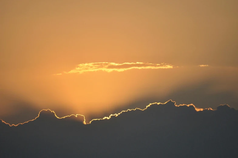 the sun rises over a hill as it peeks from clouds