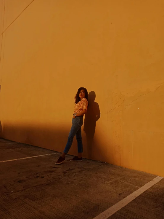 a girl leaning against a wall and looking down at her shoes