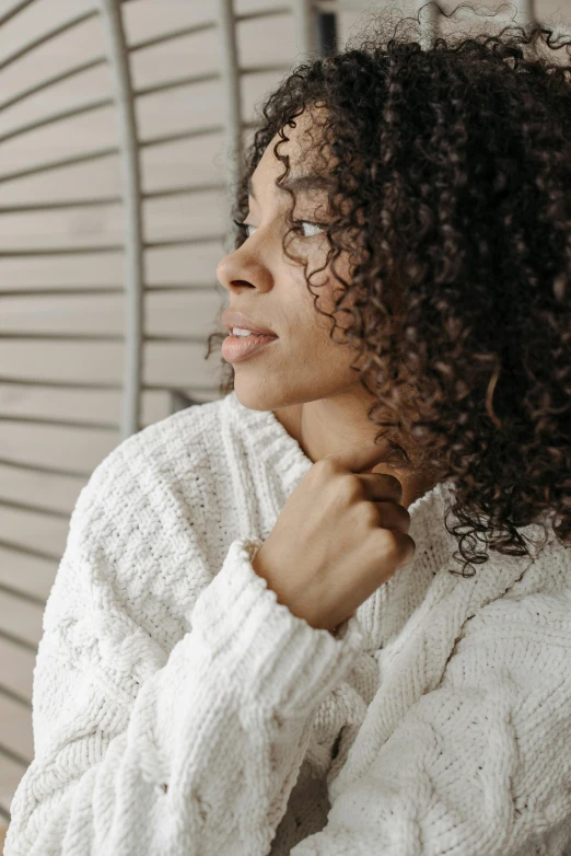 a woman with curly hair and white sweater poses for a picture