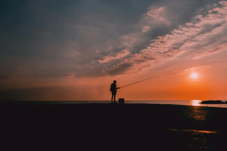 person and dog fishing in the dark on a beach at sunset