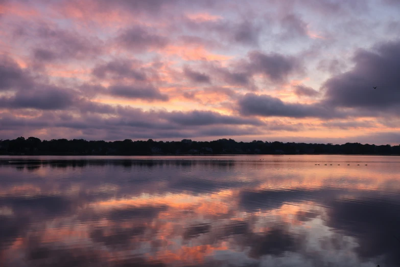 a sunset in the distance with some clouds above water