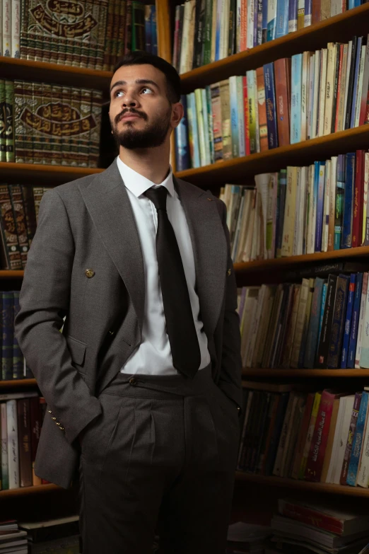 a man with a beard standing in front of a bookcase