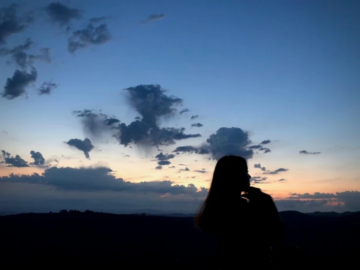 a woman on the phone while standing in front of a cloudy sunset