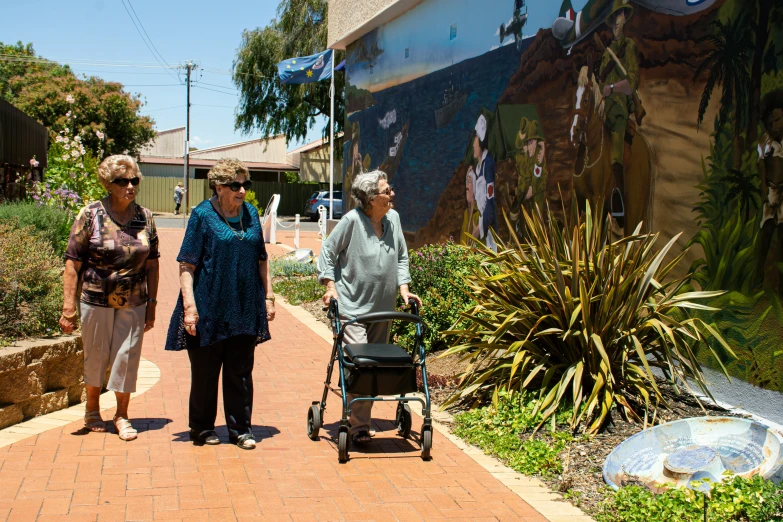 some women walking together with a baby carriage in front of a mural