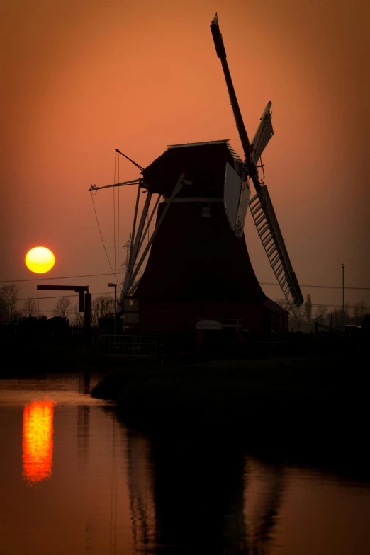 the sun is rising behind a windmill with its reflection in the water