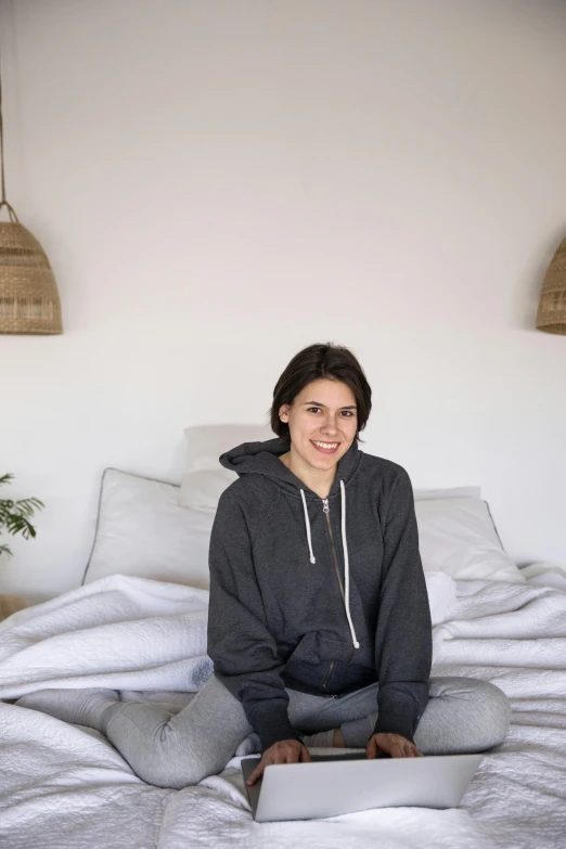 a woman sitting on a bed with a laptop computer in her lap