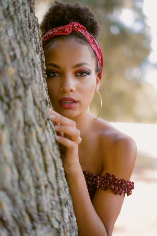 a girl wearing big hoop earrings, leaning against a tree