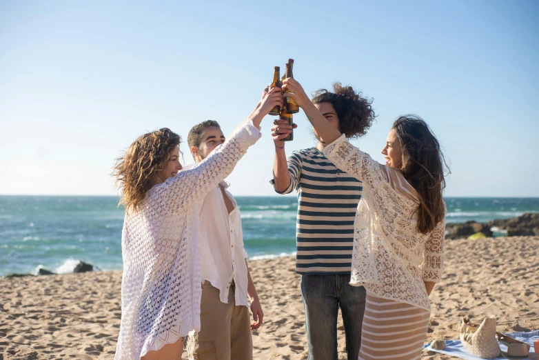 four people are standing at the beach while toasting