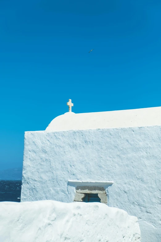 a cross atop a white building overlooking the ocean