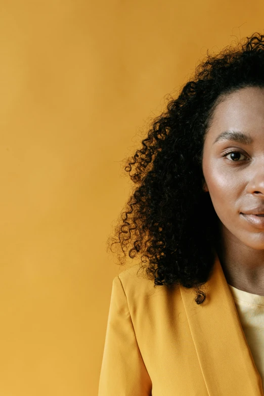 a woman with black hair and a mustard coat posing for a portrait