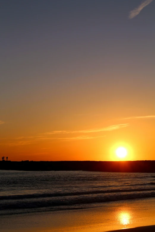 the sun rises over the ocean with a beach below