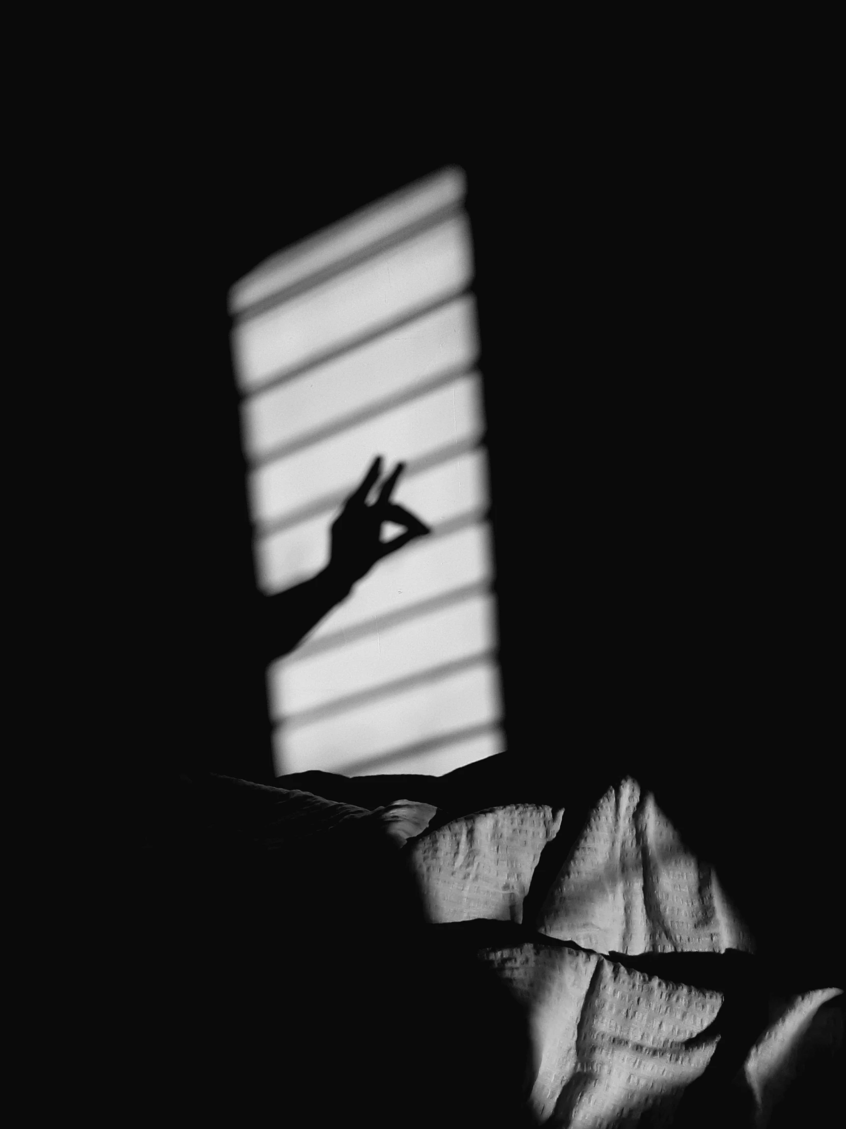 shadow cast on a dark surface with someone's hand reaching out the window
