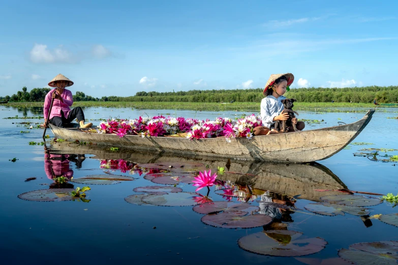 two people sitting in the middle of a small boat with water lillies