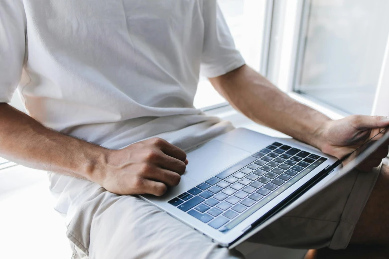 a man sits holding a laptop open and working on his hand