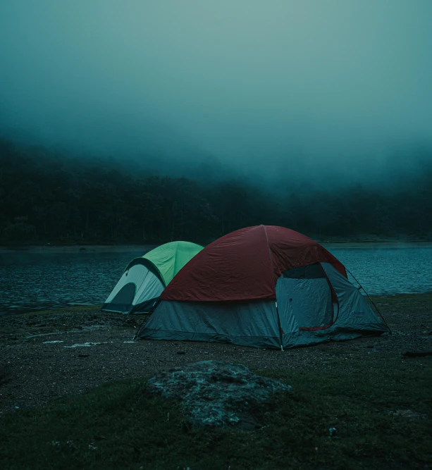 two tents set up against a misty sky near a body of water